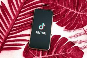 Tver, Russia-August 5, 2020, the tik tok logo on the smartphone screen on a background with green plant leaves. Tik-Tok icon. Tiktok social network. Demonstrating the colors of 2023 - Viva Magenta. photo