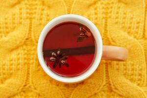 Karkade tea in an orange cup on an orange knitted background. The concept of the autumn season, natural colors. Red fruit tea. photo