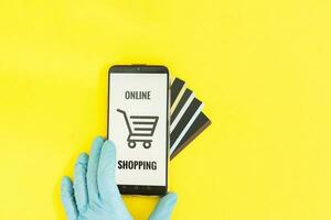 Close-up of hands in medical gloves with a smartphone. Online shopping, online banking, online payment. Payment with plastic cards. Flat Lay on a yellow background. photo