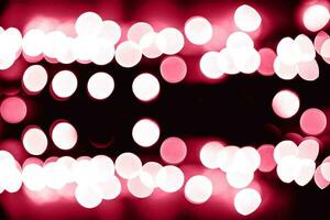 Blurry garland lights on a dark background. Festive Christmas and New Year background. Soft focus. Image toned in color of the year 2023 viva magenta photo