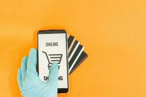 Close-up of hands in medical gloves with a smartphone. Online shopping, online banking, online payment. Payment with plastic cards. Flat Lay on a yellow background. photo