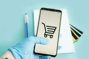 Close-up of hands in medical gloves with a smartphone. Online shopping, online banking, online payment. Payment with plastic cards. Flat Lay on blue background. photo