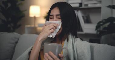 asiático joven mujer sufrimiento desde frío, enfermo con gripe, estornudos dentro pañuelo de papel desde alergias, ella tiene grave dolor de cabeza temperatura, insalubre hembra consiguiendo gripe virus síntoma frío y fiebre a hogar foto