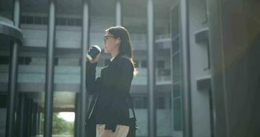 Side view shot, Footage of Young smiling elegant Asian busy business woman wearing glasses in a suit walking in front of a modern business building. Business and people concepts. video