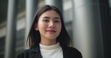 de face vue tir, métrage de Jeune souriant élégant asiatique occupé affaires femme dans une costume en marchant dans de face de une moderne affaires bâtiment. affaires et gens concepts. video