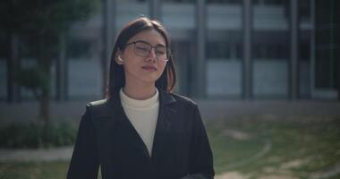 Footage of Young smiling elegant Asian busy businesswoman wearing glasses in a suit drinking coffee while standing in front of a modern business building. Business and people concepts. video