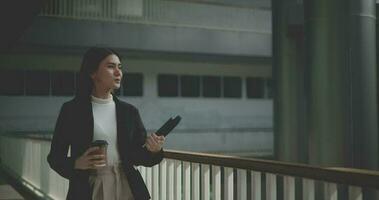 métrage de content Jeune asiatique femme d'affaires dans costume en portant une portable et tasse tandis que en marchant dans une moderne affaires bâtiment. affaires et gens concepts. video