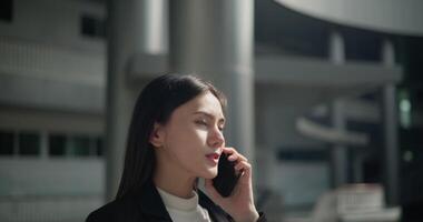 Footage of Happy young Asian businesswoman in suit talking on a smartphone while walking in a modern business building. Business and people concepts. video