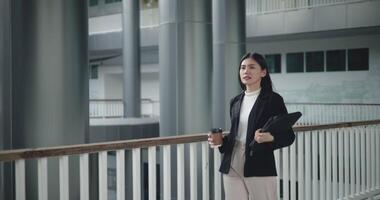 Side view shot, Footage of Happy young Asian businesswoman in suit holding a laptop and cup while walking in a modern business building. Business and people concepts. video