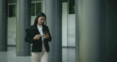 imágenes de joven asiático mujer de negocios en traje participación un ordenador portátil y taza y corriendo en un prisa en un moderno negocio edificio. negocio y personas conceptos. video