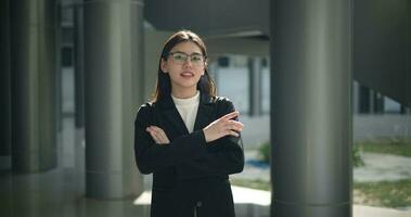 Footage of Young Asian busy businesswoman wearing glasses in a suit with crossed arms looking at the camera while standing in a modern business building. Business and people concepts. video