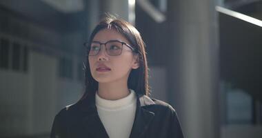 imágenes de joven elegante asiático ocupado mujer de negocios vistiendo lentes en un traje mirando a el cámara mientras en pie en frente de un moderno negocio edificio. negocio y personas conceptos. video