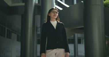 imágenes de joven asiático ocupado mujer de negocios vistiendo lentes en un traje con cruzado brazos mirando a el cámara mientras en pie en un moderno negocio edificio. negocio y personas conceptos. video