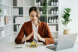 Female real estate agent is use hands to protect red roof for the concept of real estate investment about house trading, purchase at desk in office photo