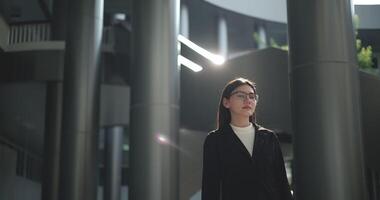 Footage of Young Asian busy businesswoman wearing glasses in a suit with crossed arms looking at the camera while standing in a modern business building. Business and people concepts. video