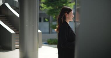 lado Visão tomada, cenas do jovem sorridente elegante ásia ocupado o negócio mulher dentro uma terno segurando uma copo do café e caminhando dentro frente do uma moderno o negócio prédio. o negócio e pessoas conceitos. video