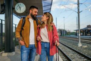 Happy couple is standing at railway station and waiting for arrival of their train. photo