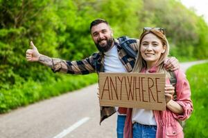 Happy couple hitchhiking on roadside trying to stop car. They are holding cardboard with inscription. photo