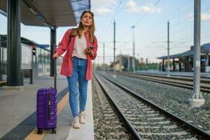 Adult woman is standing at railway station and waiting for arrival of train. photo