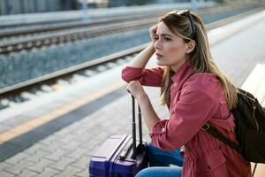 Adult woman is sitting at railway station and waiting for arrival of train. photo