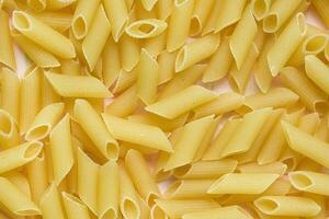 Raw Italian penne pasta on pink background photo