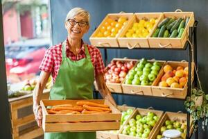 Mature woman works in fruits and vegetables shop. She is holding basket with carrot. photo