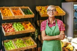 Mature woman works in fruits and vegetables shop. Portrait of small business supermarket owner. photo