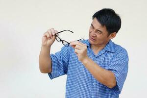 Asian man holds his eyeglasses to check because it not adjust focus with his eyesight. Concept , Eyesight health problem. Optometry. Glasses with convex or concave lenses. Myopia.Eye disease. photo