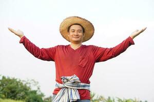 Happy Asian man farmer wears hat, red shirt, raises two hands up, feels confident. Concept, agriculture occupation, Thai farmer. Copy space of adding text or advertisement. photo