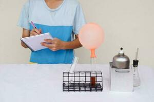 Closeup student writes on paper, observes, do science experiment about balloon. Concept, Action research. Science project work activity. Learning by doing and observing. Education. Self study. photo