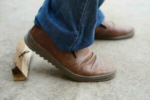 Closeup man wears shoes is stepping on rusty metal nail on wood. Concept, unsafe , risk for dangerous tetanus. Be careful and look around during walking at construction site or risk places. photo