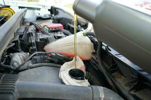 Pouring oil to the car. Car mechanic holding a bottle of oil in hand over the engine. Car engine oil. Topping up car oil. photo