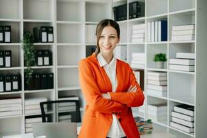 Confident business expert attractive smiling young woman typing laptop ang holding digital tablet on desk in office. photo