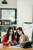 Two Asian businesswoman discuss investment project working and planning strategy with tablet laptop computer in office. photo