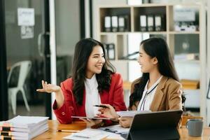 Two Asian businesswoman discuss investment project working and planning strategy with tablet laptop computer in office. photo