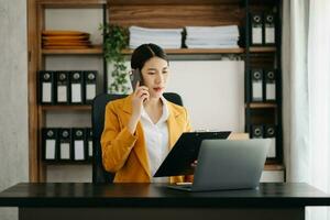 mujer de negocios asiática tiene la alegría de hablar en el teléfono inteligente, tableta y computadora portátil en la oficina moderna foto