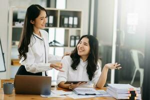 Two Asian businesswoman discuss investment project working and planning strategy with tablet laptop computer in office. photo