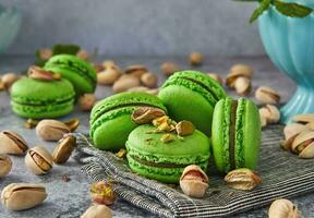 Green colored pistachio macarons with pistachios and mint on gray wooden background photo