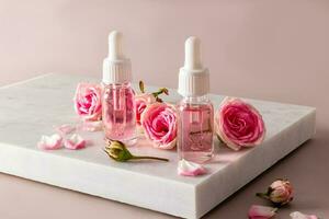 Natural rose petal oil or oil-based serum in two cosmetic bottles on a white marble podium. natural cosmetics. care. photo