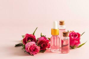 Serum with rose petals and rose water in glass bottles against a background of live pink roses. A fashionable cosmetic product for young skin. photo