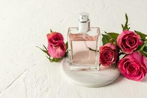 un elegante vaso botella de perfume o eau Delaware baño soportes en un redondo mármol podio con té rosas. presentación de el fragancia. un Copiar espacio foto