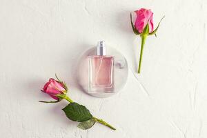 Beautiful perfume bottle with the aroma of delicate roses on a white round podium with roses. Top view. Flat styling. white textured background. photo