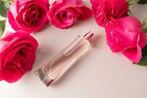 A transparent bottle of women's perfume or eau de toilette lies among the large buds of pink roses. Top view. Template for product presentation. photo