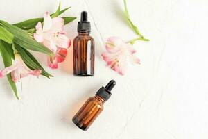 face and body skin care product, essential oil, serum in two cosmetic bottles with a dropper on a white background with astromeria flowers. Top view. photo