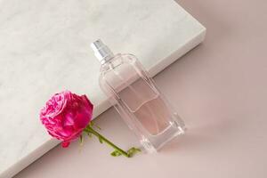 cosmético perfume producto rociar en un transparente hermosa botella inclinado en un blanco pedazo de mármol con un rosado Rosa. producto presentación. foto