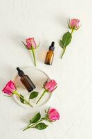 Two cosmetic bottles with dropper with a multifunctional serum on a white background with fresh roses. Top view. Flat lay. natural cosmetics. photo