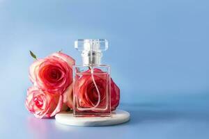 crystal bottle of women's perfume with the aroma of delicate roses on a blue background with pink fresh roses. The front view. copy space. photo