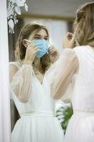 The bride in the medical mask looks in the mirror. photo