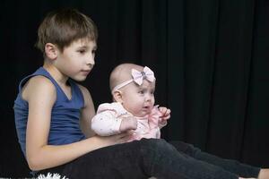 The older brother holds the little sister on his lap. photo