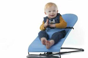 A cute toddler sits in a baby lounger and smiles on a white background. A beautiful one-year-old child. photo